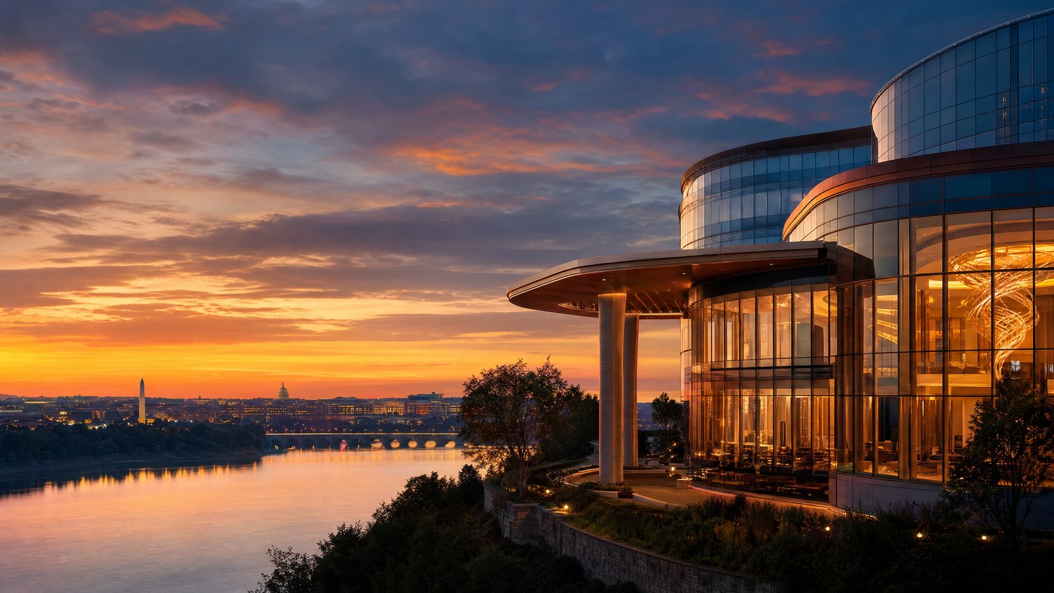 A modern glass hotel overlooking the Potomac River and Washington-area skyline at sunset.