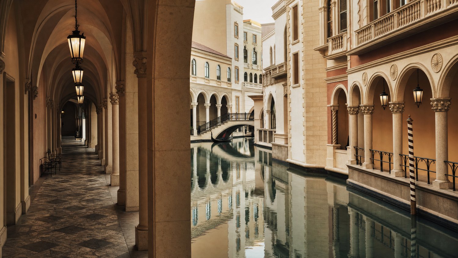 A calm Italianate canal passage framed by arches and stone colonnades.